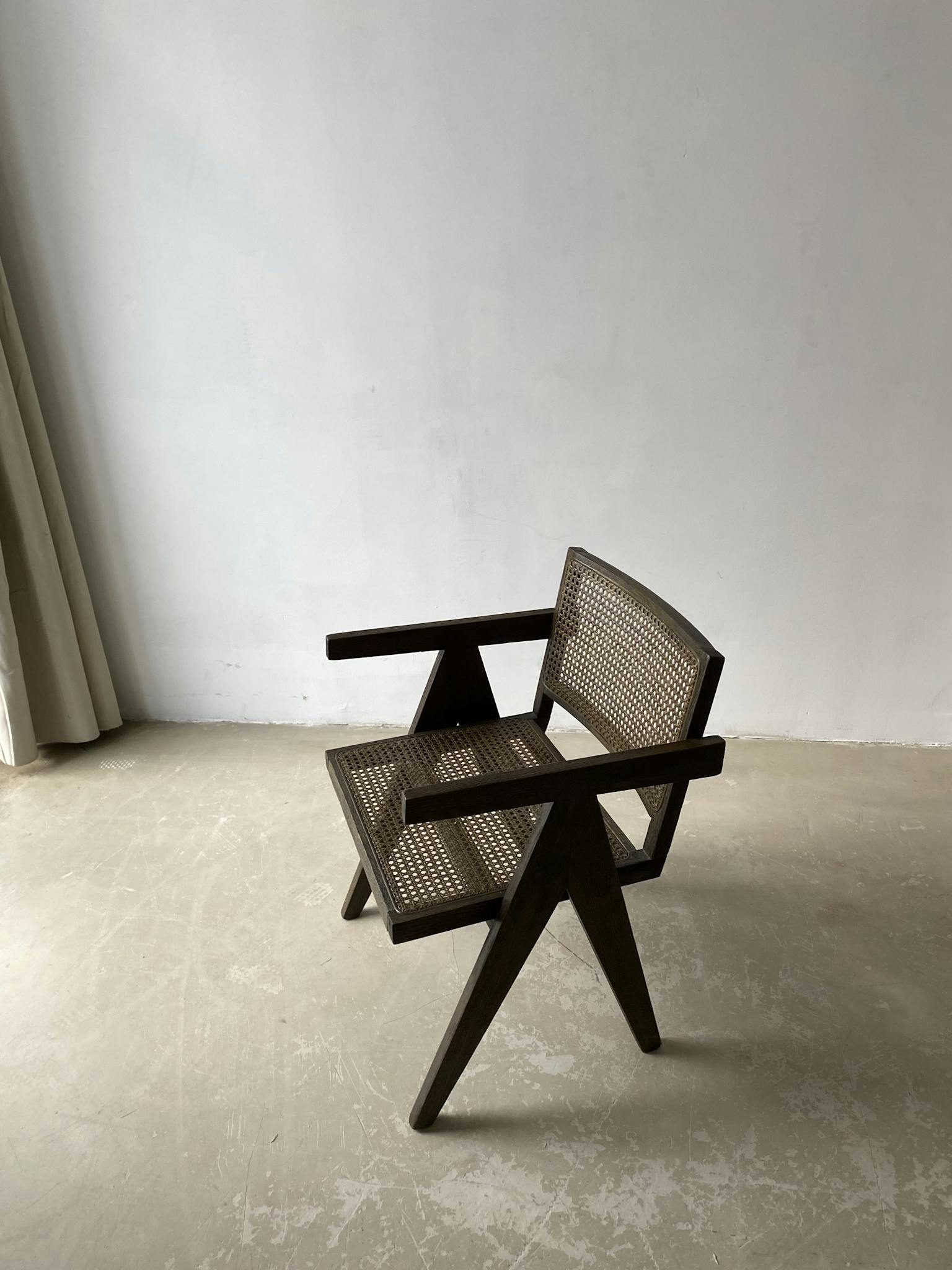 A modern wooden cane armchair with angular design against a neutral wall.